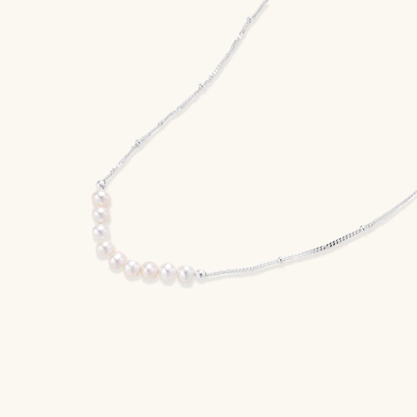 Delicate sterling silver chain necklace with small freshwater pearls arranged in a curved smile arc on cream background.