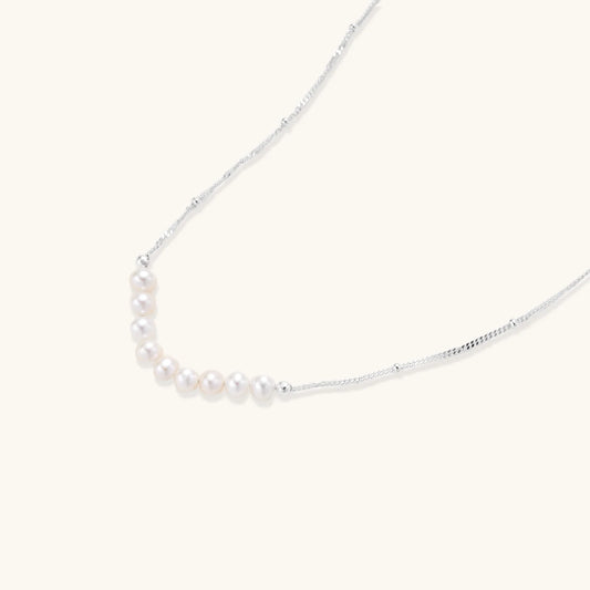 Delicate sterling silver chain necklace with small freshwater pearls arranged in a curved smile arc on cream background.