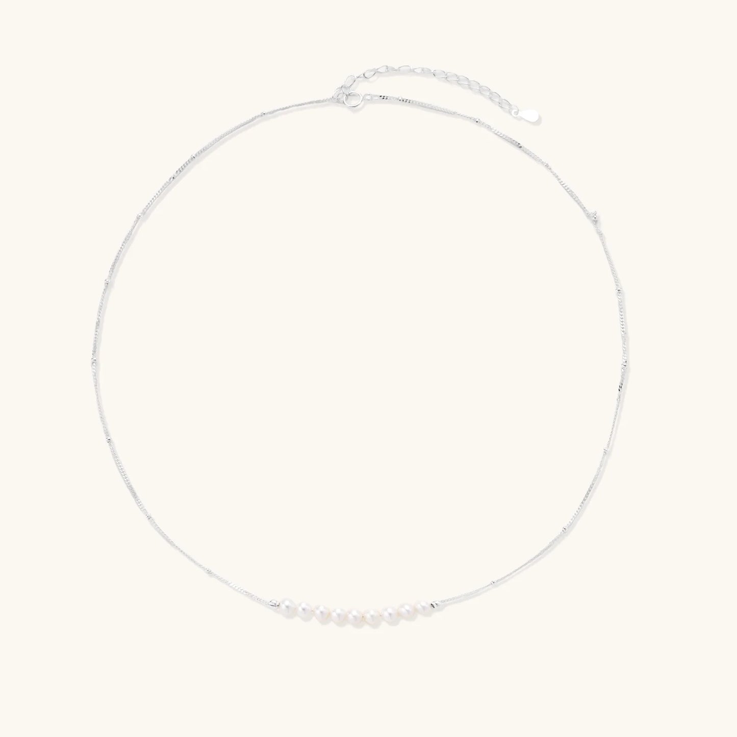 Delicate sterling silver chain necklace with small freshwater pearls arranged in a curved smile arc on cream background.