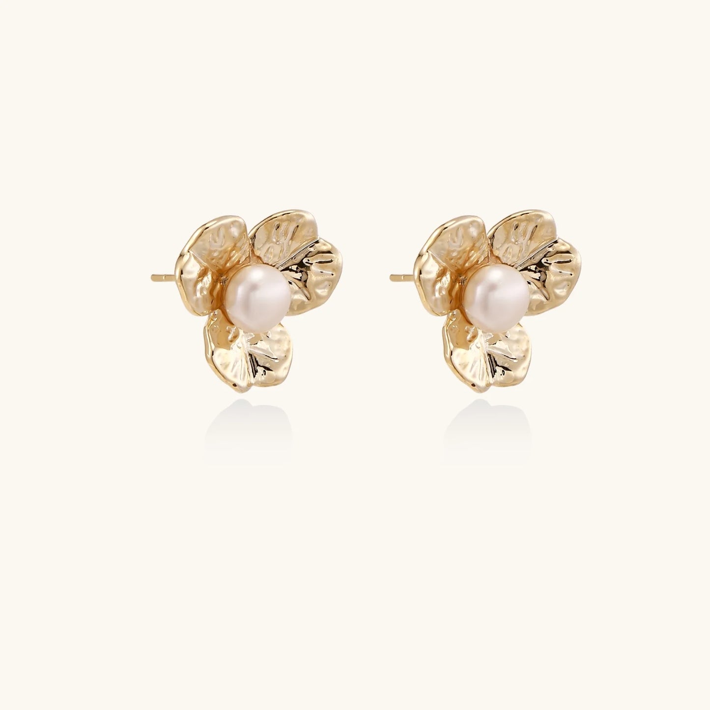 Gold-plated flower stud earrings with textured petals and centered freshwater pearl on beige background