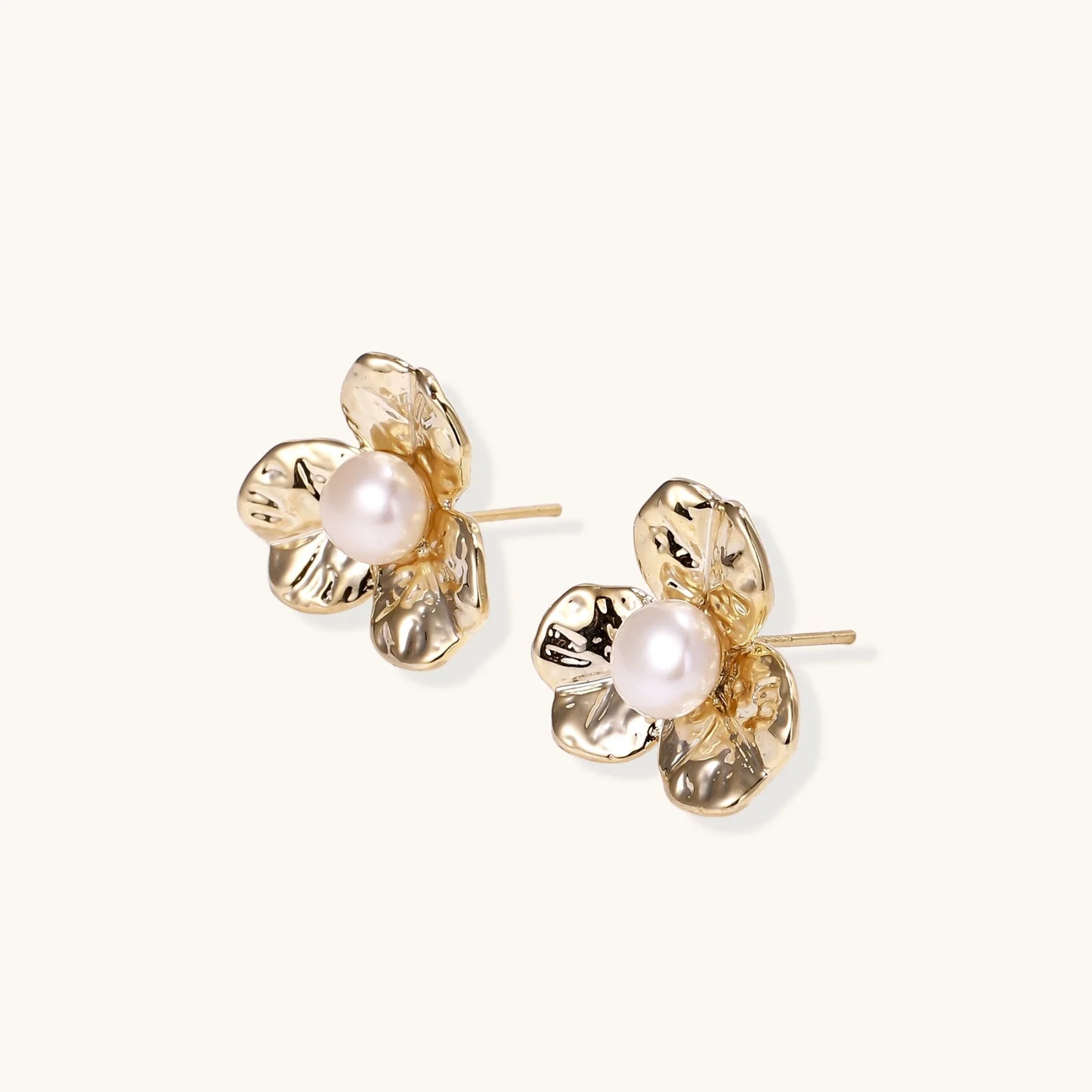 Gold-plated flower stud earrings with textured petals and centered freshwater pearl on beige background