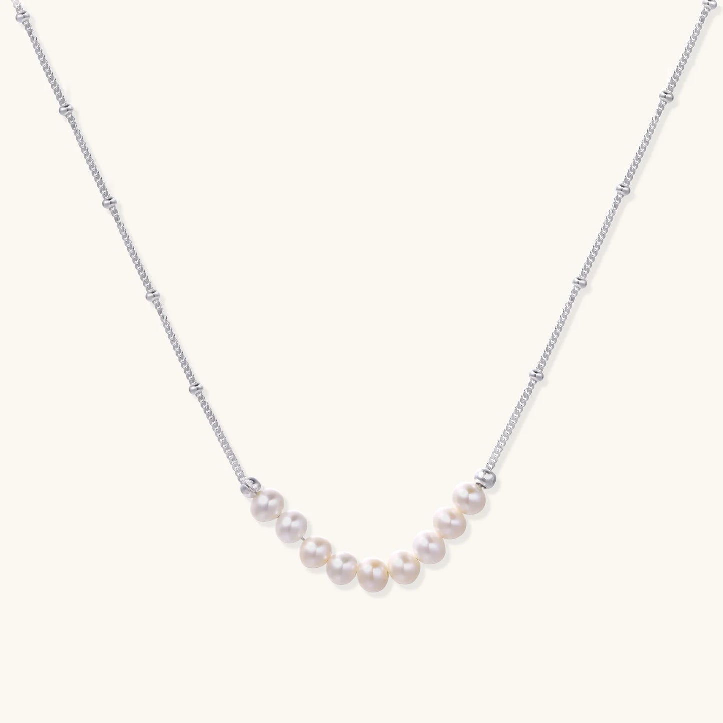 Delicate sterling silver chain necklace with small freshwater pearls arranged in a curved smile arc on cream background.