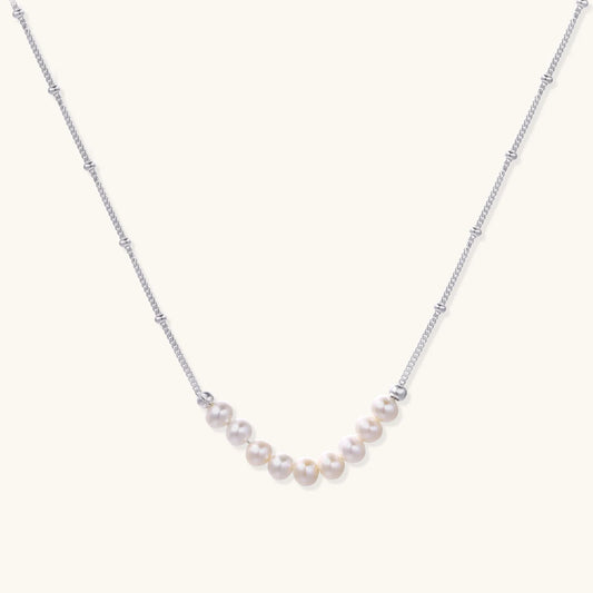 Delicate sterling silver chain necklace with small freshwater pearls arranged in a curved smile arc on cream background.